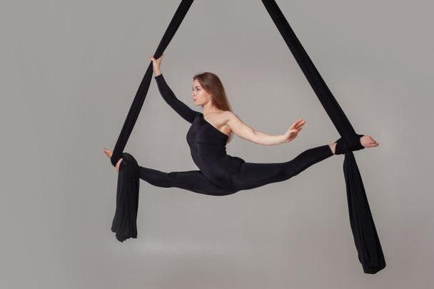 Hermosa chica en un traje deportivo negro está realizando un acrobático elementos en un estudio
. - Foto, Imagen