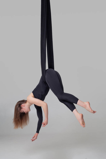 Beautiful girl in a black sport suit is performing an acrobatic elements in a studio. - Foto, Bild