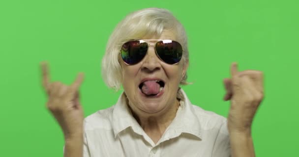 Μια ηλικιωμένη γυναίκα δείχνει σημάδια από τα κέρατα με τα χέρια της και δείχνει τη γλώσσα - Πλάνα, βίντεο