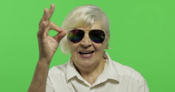 Güneş gözlüğü yaşlı bir kadın ok jest göstermek ve gülümsüyor. Chroma anahtarı - Video, Çekim