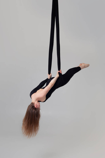 Beautiful girl in a black sport suit is performing an acrobatic elements in a studio. - Foto, imagen