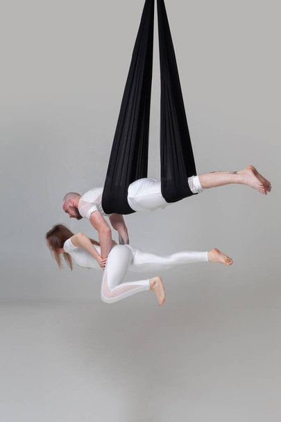 Beautiful girl and an athletic man in a white sport suits are performing an acrobatic elements in a studio. - Photo, Image
