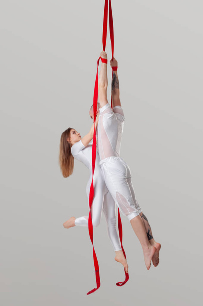 Красивая девушка и атлетичный мужчина в белых спортивных костюмах исполняют акробатические элементы в студии
. - Фото, изображение