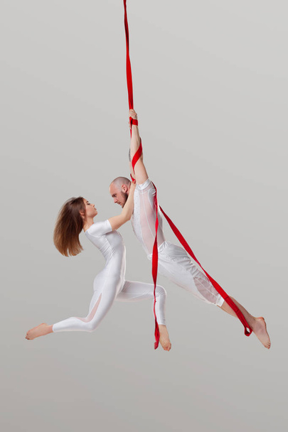 Beautiful girl and an athletic man in a white sport suits are performing an acrobatic elements in a studio. - Foto, immagini