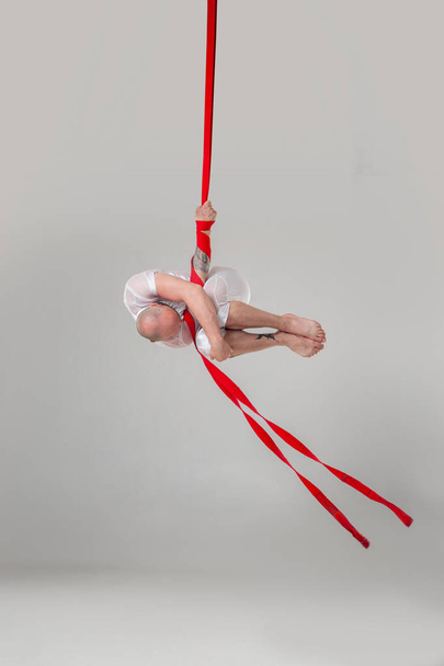 Sportos férfi egy fehér sport öltönyt végez akrobatikus elemek egy stúdióban. - Fotó, kép