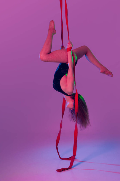 Beautiful girl in a black swimsuit is performing an acrobatic elements in studio. - Photo, Image