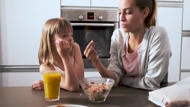 schöne Mutter und ihre Tochter, die zu Hause in der Küche Müsli von der Schüssel nimmt und isst. - Filmmaterial, Video