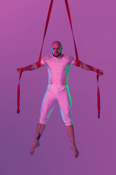 Athletic man in a white sport suit is performing an acrobatic elements in a studio. - Photo, Image