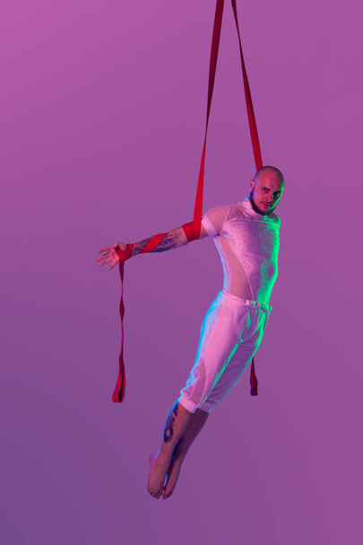 Athletic man in a white sport suit is performing an acrobatic elements in a studio. - Photo, Image