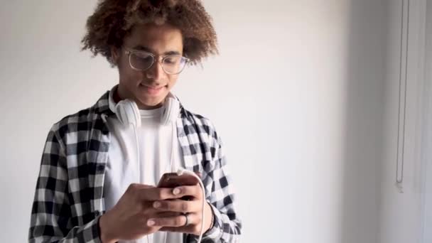 Красивый молодой африканский американец пользуется своим мобильным телефоном дома. Изолированный на белом фоне
. - Кадры, видео