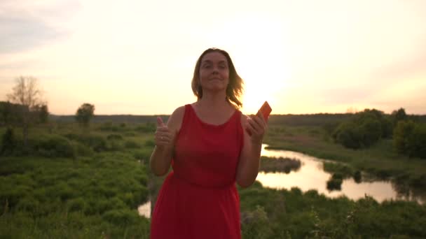 urkomische Frau tanzt mit ihrem Handy am kleinen Rohrweiher bei Sonnenuntergang in Slo-mo - Filmmaterial, Video