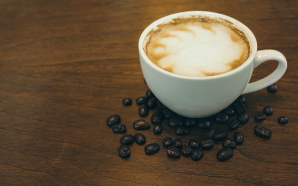 Filiżanka kawy i ziarna kawy na drewnianym stole w kawiarni - Zdjęcie, obraz