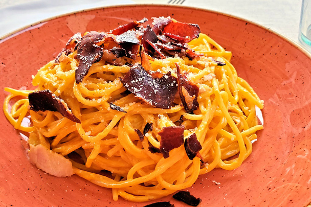 Espagueti carbonara italiano fresco con tocino crujiente y queso parmesano. Vista de cerca en una placa de color rosa
. - Foto, Imagen