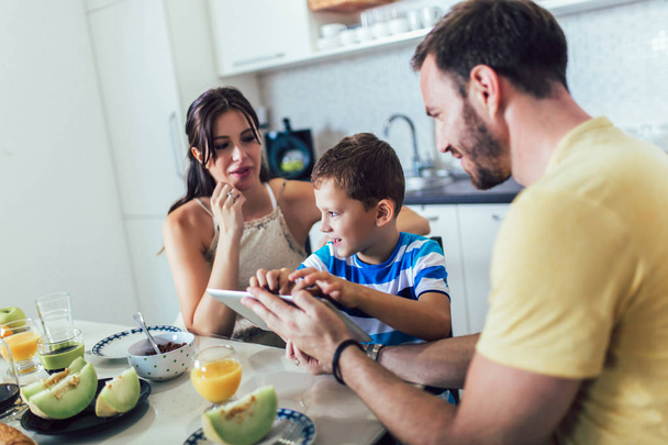 Família tomando café da manhã na mesa da cozinha e usando mesa digital
 - Foto, Imagem