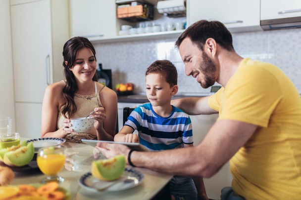 キッチンテーブルで朝食を食べ、デジタルテーブルを使用する家族 - 写真・画像