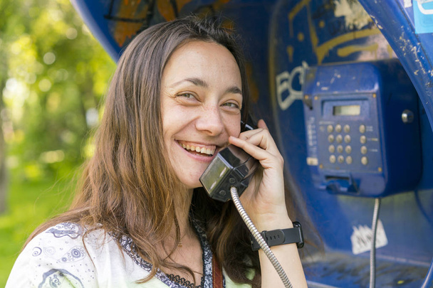 Krásná mladá žena v telefonní budce. Ta holka mluví po telefonu z telefonní budky. hezká žena, mluvící veřejným telefonem - Fotografie, Obrázek