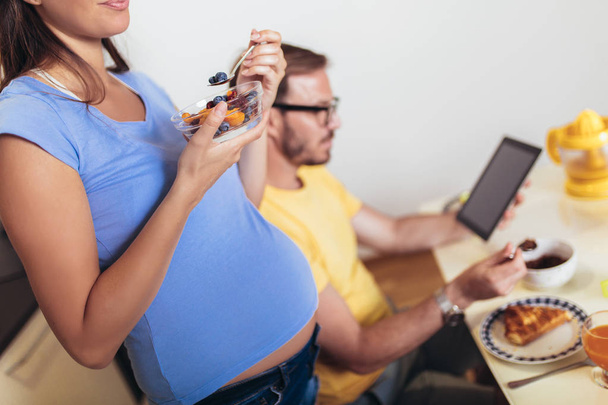 Έγκυος γυναίκα με τον άντρα στην κουζίνα χρησιμοποιώντας ψηφιακό δισκίο. - Φωτογραφία, εικόνα