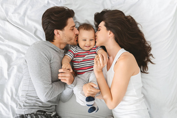 Felice coppia caucasica baciare dolci guance del loro adorabile bambino figlio
 - Foto, immagini