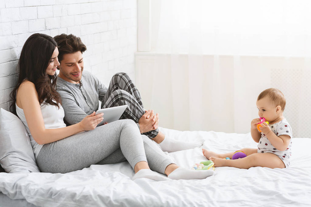 Moeder en vader netwerken op digitale Tablet, kleine baby spelen alleen - Foto, afbeelding