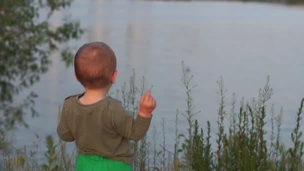 Miły blond dzieciak stojący i rzucanie chleba do kaczek w jeziorze o zachodzie słońca w SLO-mo - Materiał filmowy, wideo
