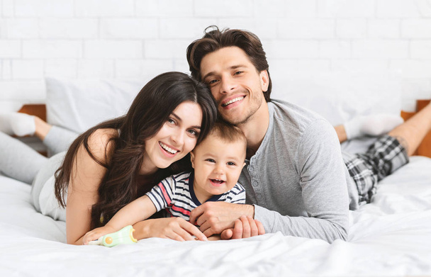 Happy millennial family bonding on bed with baby - 写真・画像