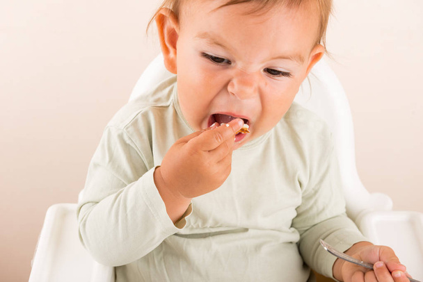 Baby toddler eats food with fingers. Fun face. Copy space - Foto, imagen