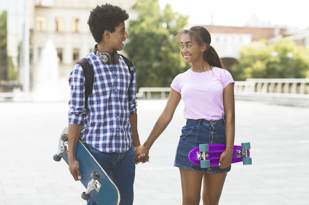 Adolescente casal com skates de mãos dadas andando ao longo da rua da cidade
 - Foto, Imagem