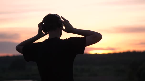 Vidám ember áll a fülhallgató és integetett a kezét a kis tó naplementekor a slo-Mo - Felvétel, videó