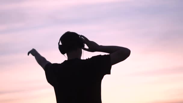 glücklicher Mann mit Kopfhörern und erhobenen Händen am kleinen See bei Sonnenuntergang im Slo-mo - Filmmaterial, Video