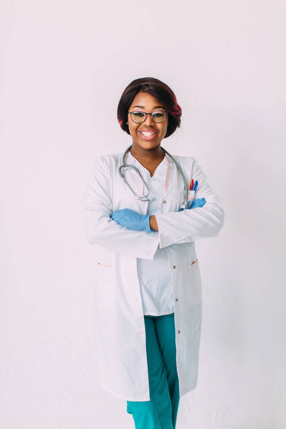 Young smiling African American woman doctor in medical gloves and clothes, isolated on white - Foto, Imagen