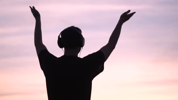 Vidám ember áll a fülhallgató és a kapaszkodó kezét a tó naplementekor a slo-Mo - Felvétel, videó