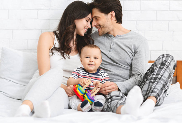Boldog szülők kötés, imádnivaló baba játszik a játék - Fotó, kép