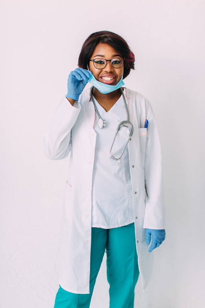 Young smiling African American woman doctor in medical mask and blue gloves, isolated on white background - Zdjęcie, obraz