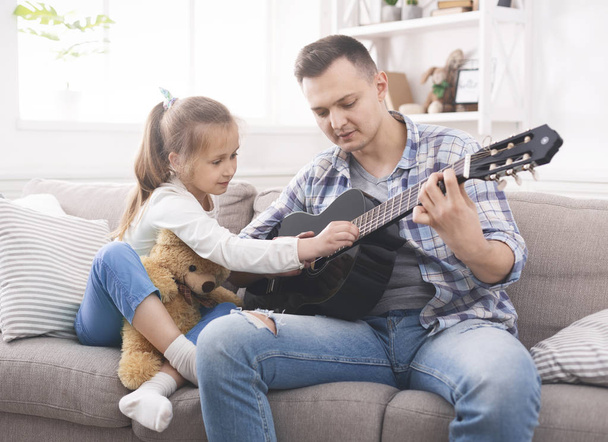 Cute little girl is helping her father to play guitar - Zdjęcie, obraz