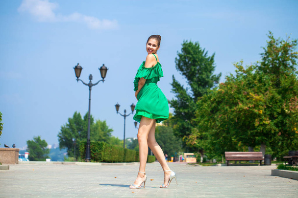 Young beautiful woman in green dress walking on the summer stree - Фото, изображение