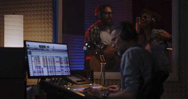 Τραγουδιστής κιθαρίστας και μηχανικός ήχου που εργάζονται στο στούντιο - Φωτογραφία, εικόνα