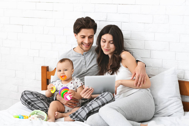 Parents naviguant sur tablette numérique, assis sur le lit avec bébé fils
 - Photo, image