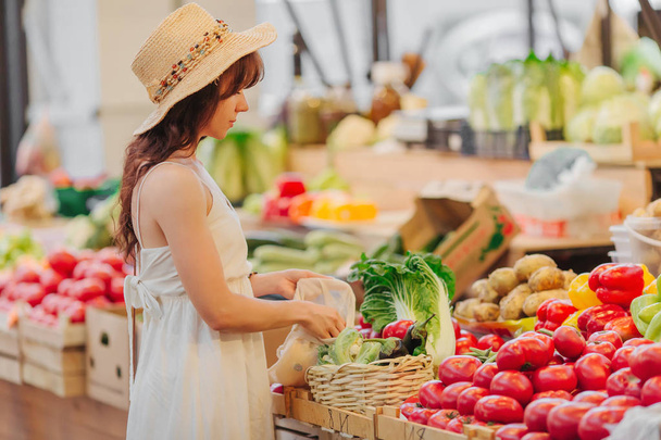 Mujer joven pone frutas y verduras en bolsa de algodón en el mercado de alimentos. Bolsa ecológica reutilizable para ir de compras. Concepto de cero residuos
. - Foto, imagen