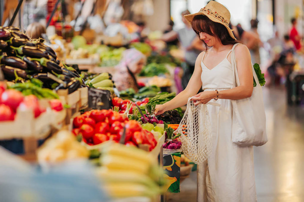 Young Woman puts fruits and vegetables in cotton produce bag at food market. Reusable eco bag for shopping. Zero waste concept. - Φωτογραφία, εικόνα