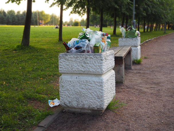 Πλημμυρισμένη σκουπιδοτενεκέδες στο πάρκο γεμάτα από όλα τα σκουπίδια. Οι άνθρωποι αφήνουν πίσω τα σκουπίδια. Ρύπανση του περιβάλλοντος. Οικολογικό πρόβλημα αποβλήτων πλαστικών. - Φωτογραφία, εικόνα