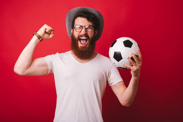 Портрет счастливого человека с бородой, держащего футбольный мяч и празднующего
 - Фото, изображение