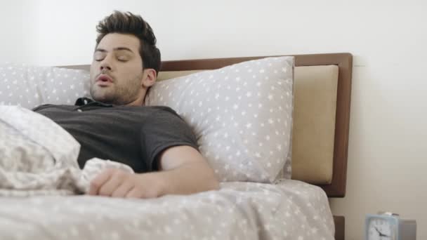 schläfriger Mann wacht morgens im Schlafzimmer auf. schöner Kerl schaltet Wecker aus - Filmmaterial, Video