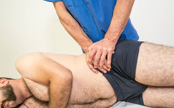Doktor fizyoterapist bir fizyoterapi odasında hastanın egzersiz iliac corection yaparken bir erkek hastaya yardımcı, rehabilitasyon fizyoterapi kavramı. - Fotoğraf, Görsel