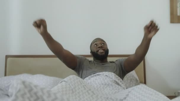 Jonge kerel uitgerekt armen in bed in de ochtend. Zwarte man dansen in bed. - Video