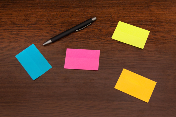 Beautiful colorful sticky notes and pen on brown wooden desk. Top view and space for text. Close up, selective focus - Photo, Image