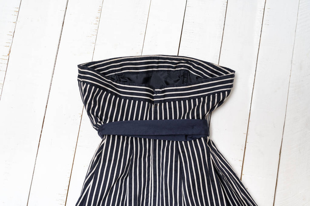 Clothes fashion concept. Detail of blue striped dress with bow on white wooden background. Top view - Photo, Image