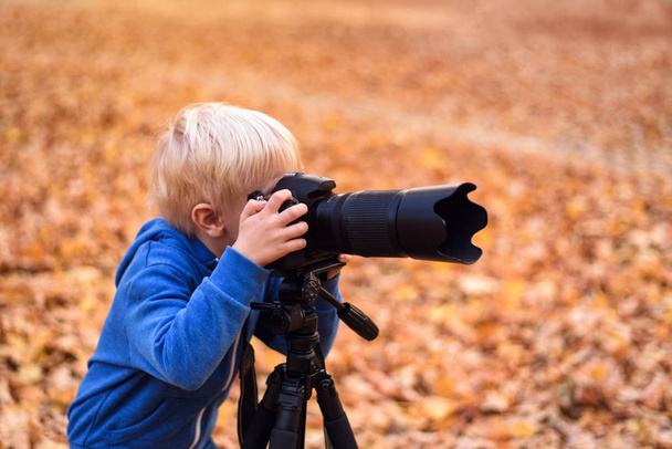 El niño rubio toma fotos en una cámara SLR. Parque de otoño
 - Foto, Imagen