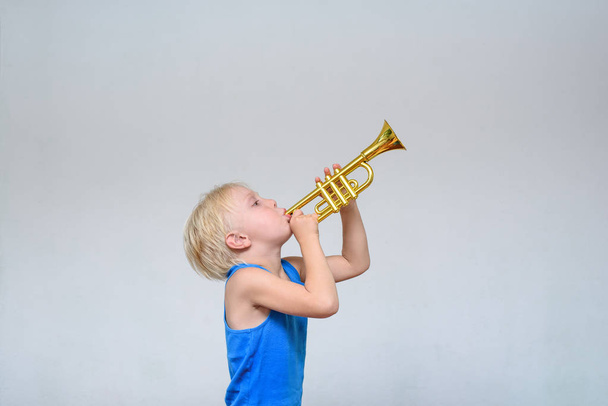 Kleine schattige blonde jongen spelen speelgoed trompet op lichte achtergrond - Foto, afbeelding