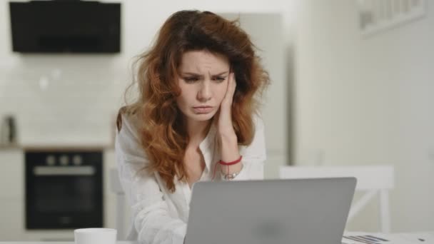 Απογοητευμένη γυναίκα που δουλεύει στον υπολογιστή στο σπίτι. Νεαρή κυρία κοιτάζοντας φορητό υπολογιστή στην κουζίνα. - Πλάνα, βίντεο