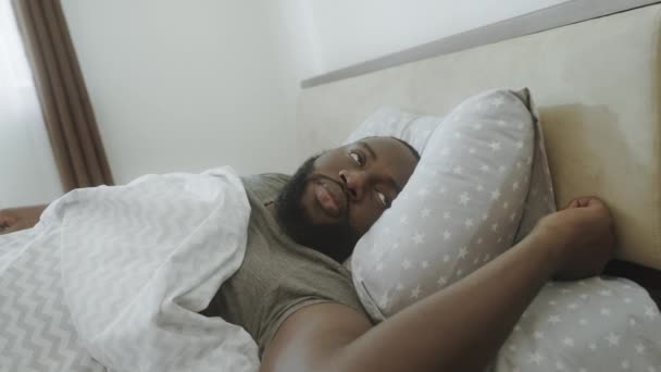 Zwarte man luisteren geluid in de ochtend. Geïrriteerde mannelijke persoon die wakker wordt in bed. - Video
